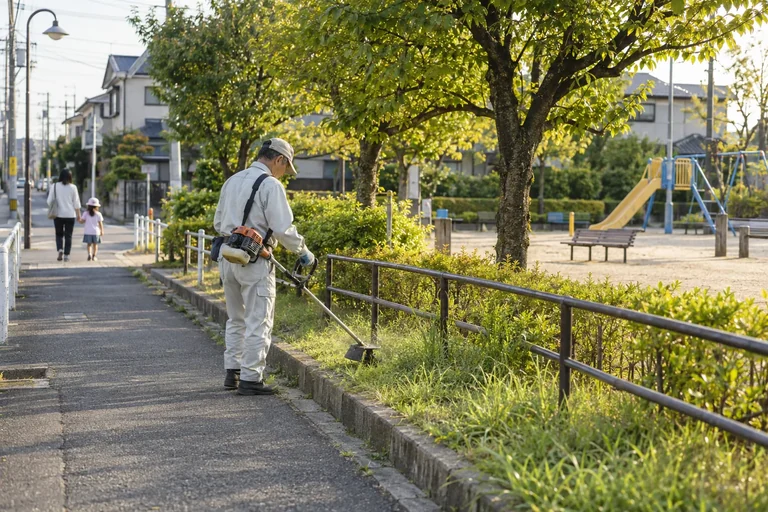 公園に隣接する歩道の草を刈る作業員
