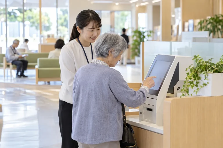 公共施設の案内端末を職員と操作する高齢の利用者